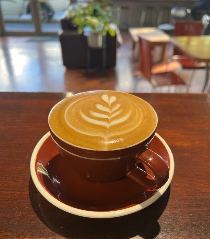A flat white with leaf latte art in a brown cup